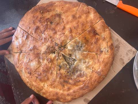       A freshly baked round bread sliced into pieces with a hand visible.
  