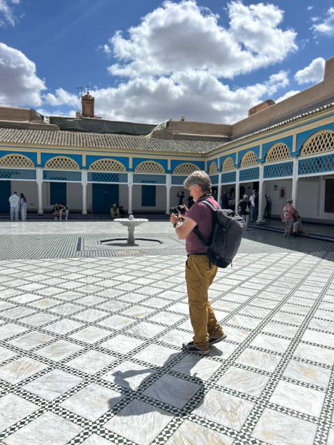       A man taking a photo in a courtyard with decorative tilework.
  