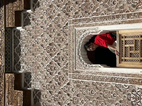      Woman looking out from a decorative window in a historic building.
  