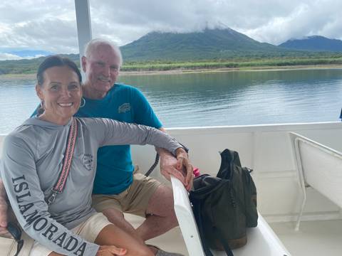A couple on a boat with a scenic view of a lake and volcano in the background.