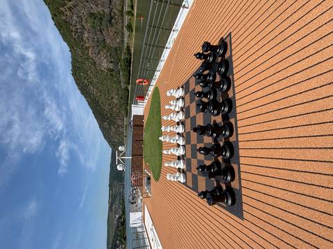 A giant chess set on a cruise ship with a scenic background.