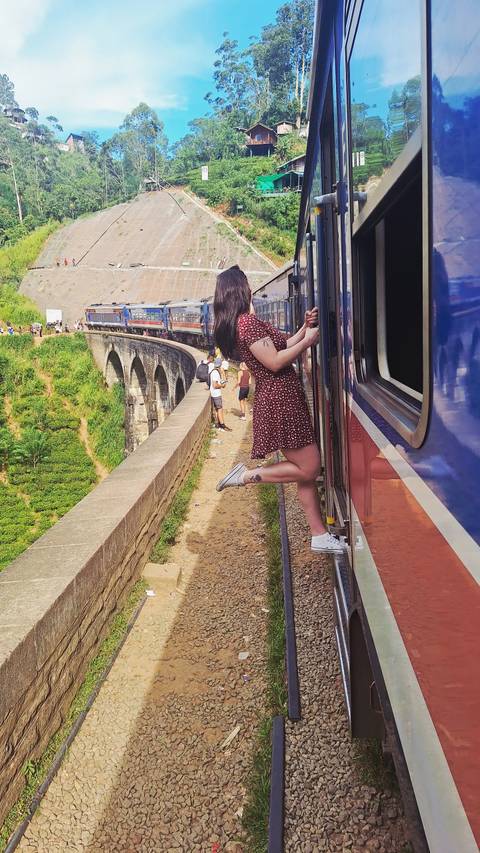People leaning out of a train traveling over a scenic viaduct.