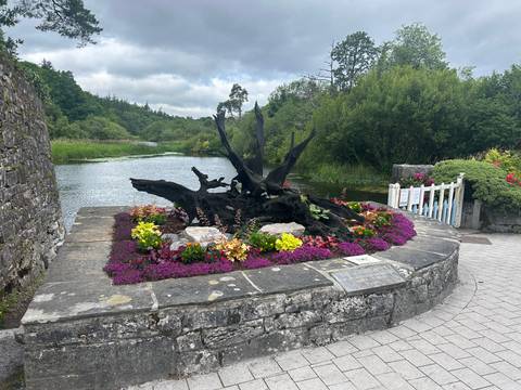 A scenic view of a stone monument surrounded by vibrant flowers by a river.