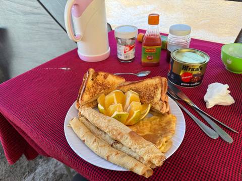 Breakfast plate with toast, omelette, orange slices, and hot drinks on a red tablecloth.