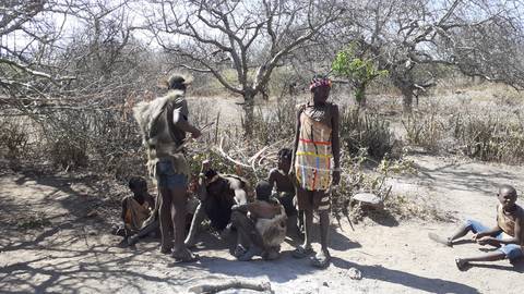       Group of indigenous people sitting and standing in a rural setting.
  