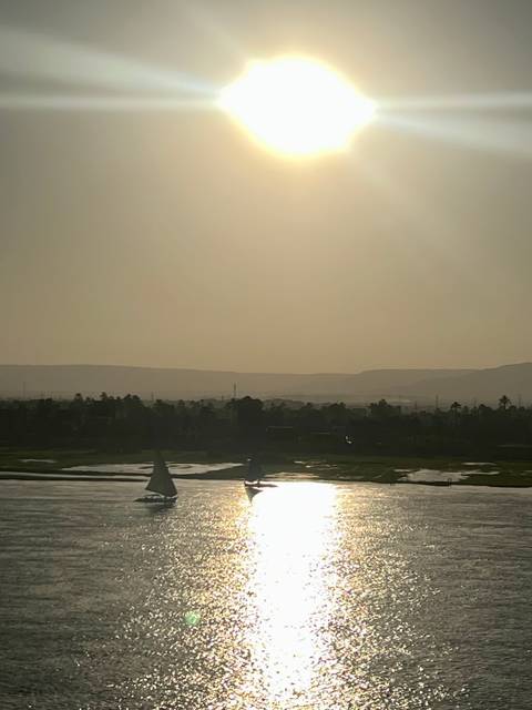 River view with silhouettes of boats and a hazy skyline at sunset.