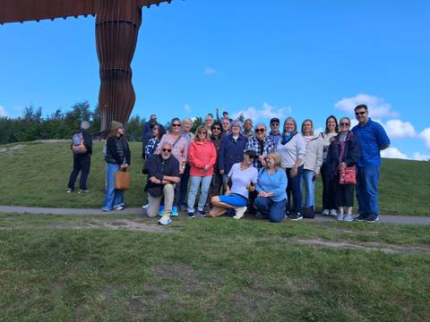       Group of tourists posing outside with a large sculpture in the background.
  