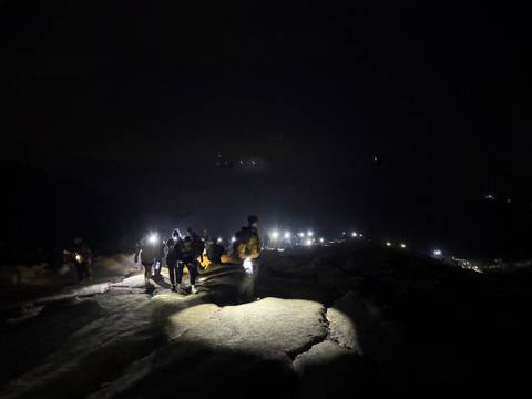       Group of people hiking at night with headlamps illuminating a rocky terrain.
  