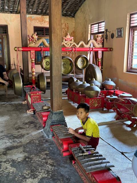       Child surrounded by traditional musical instruments indoors.
  