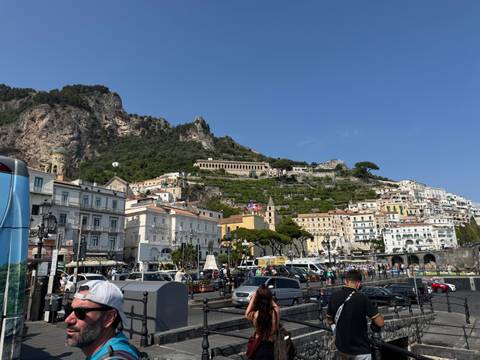       Busy street in a coastal town with people and buildings.
  