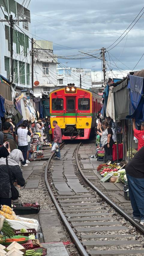       Train passing through a busy marketplace with people taking photos.
  