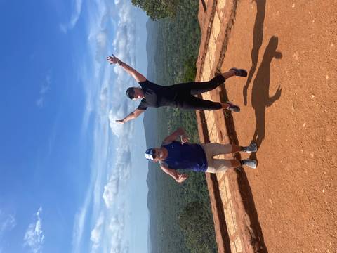 Two people jumping on a hill with a scenic background.