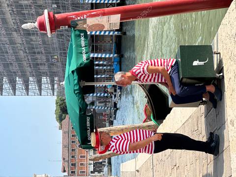       Gondoliers in striped shirts by a canal.
  