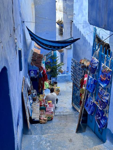       A blue street with shops and a person sitting.
  