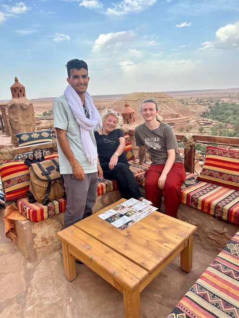       Three people sitting with a view of Ait Benhaddou in the background.
  