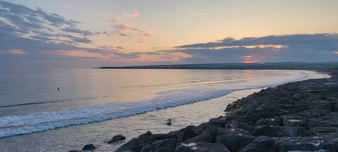       A serene beach at sunset with gentle waves and rocky shoreline.
  