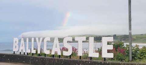       Sign for Ballycastle with a rainbow in the background.
  
