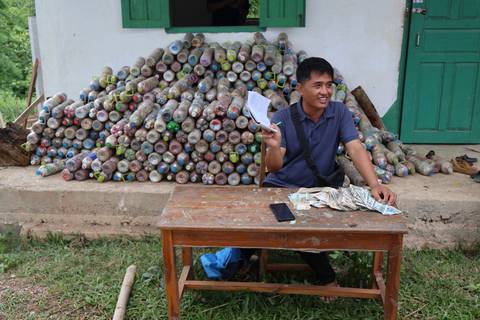 A person sitting at a table with a pile of hollow bottles in the background.