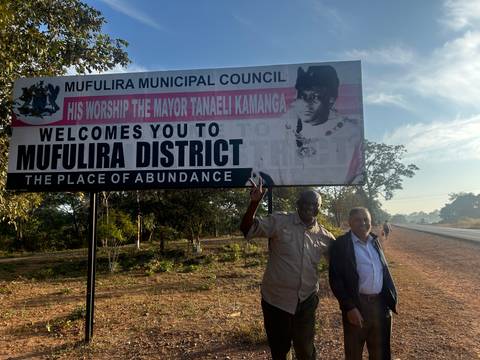 Two men standing in front of a district welcome sign.