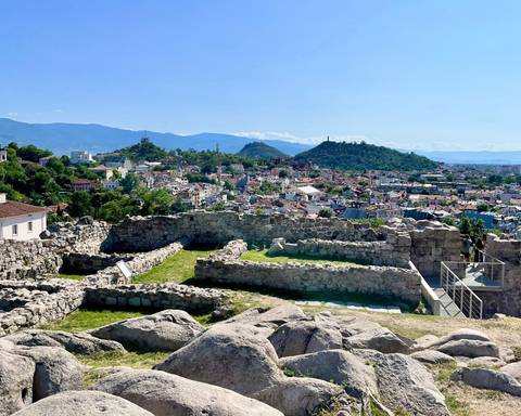       Panoramic view of ancient ruins with a cityscape and mountains in the background.
  