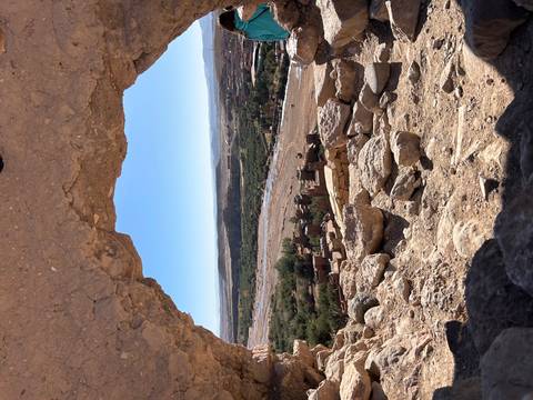       View through a rock frame of a lush green valley with a village and fields.
  