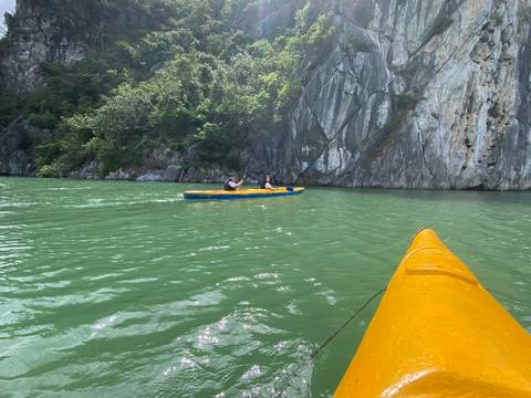 Two kayakers paddling in green waters next to rocky cliffs.
