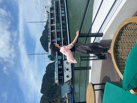 A woman standing on a cruise deck with a view of the sea and another boat.