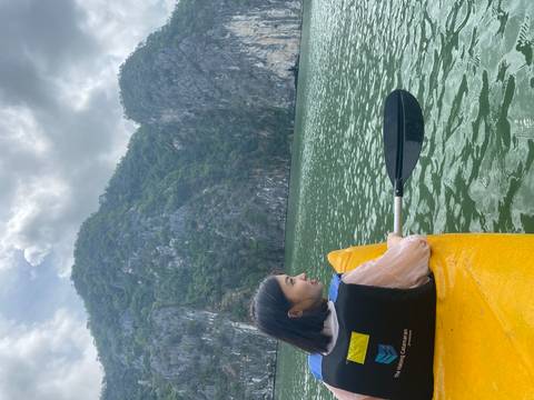 A woman kayaking in turquoise waters with green cliffs in the background.