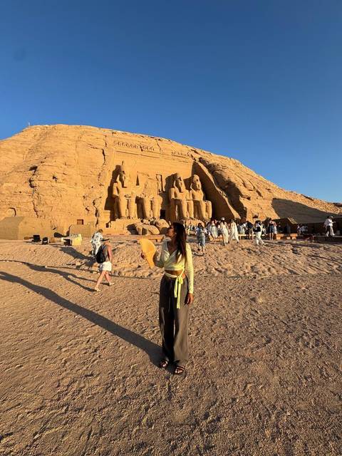 A woman holding a fan in front of Abu Simbel.