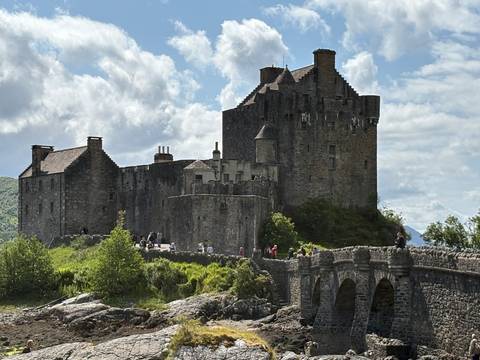 A medieval castle with a stone bridge and people around.