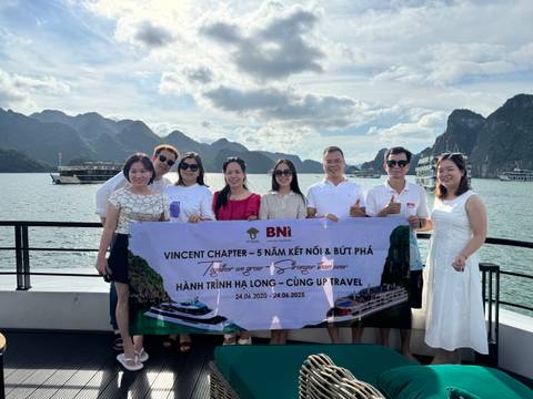 A group of people holding a banner on a boat with limestone karsts in the background.