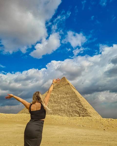 Person reaching toward a pyramid under a dramatic sky.