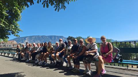       A large group of people sitting on a bench with a mountainous backdrop.
  