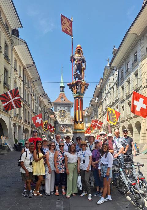      Tourists posing in a historic street with Swiss flags.
  