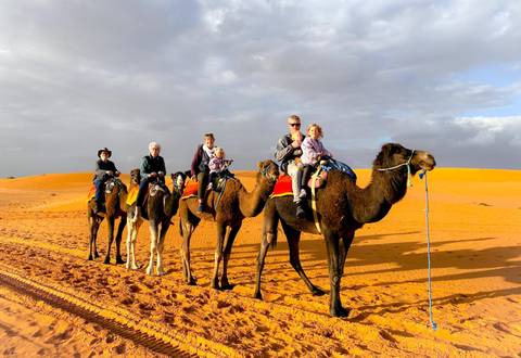 Tourists riding camels through the desert at sunset.