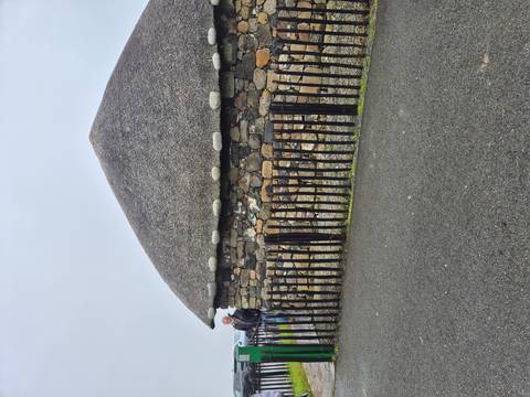 Person standing near a stone building with a thatched roof.