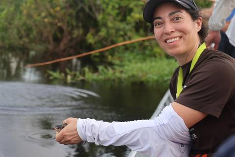 Smiling woman holding a small alligator by the water.
