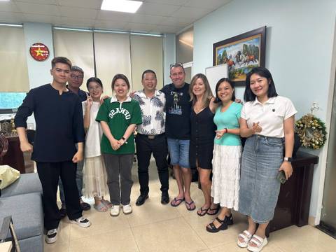 Group of people posing indoors with framed artwork in the background.