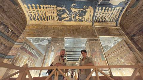 Two people inside a tomb with detailed ceilings in Egypt.