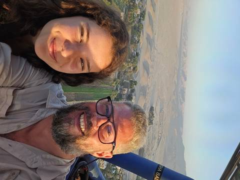Selfie of two people in a hot air balloon over desert landscape.