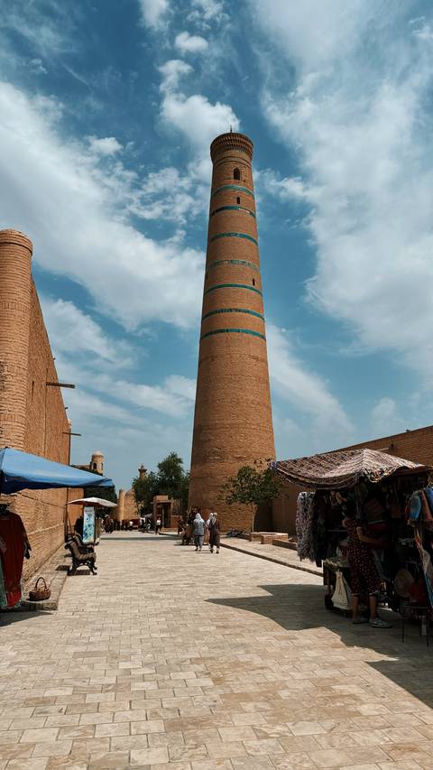       Minaret with blue bands against a partly cloudy sky.
  