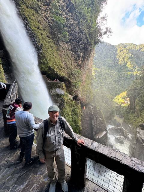       People visiting a waterfall in a lush forest setting.
  