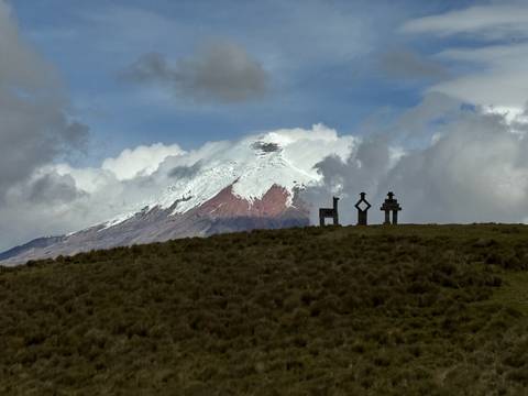       Volcano with snow cap seen from a grassy hill with three sculptures.
  