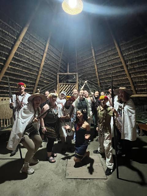       Group dressed in traditional attire posing inside a hut.
  