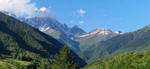 Snow-capped mountains with lush green valley under blue sky.