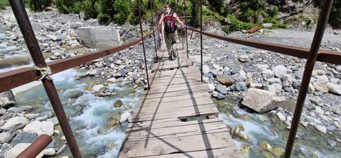 Person crossing a wooden bridge over a rocky river.