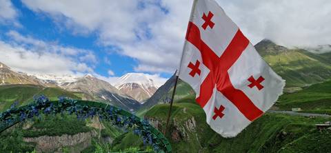 Flag of Georgia with mountains in the background.