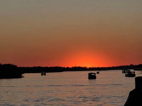 Sunset over a river with small boats silhouetted.
