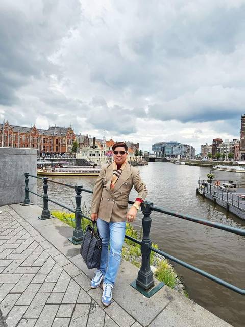 Person posing on a railing with a cityscape and river in the background.