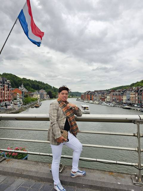 Person standing on a bridge overlooking a scenic town and river.